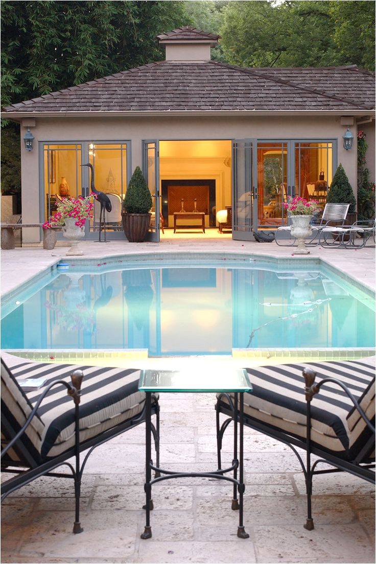 view of a lighted pool house next to an inground swimming pool with two loungers in the foreground