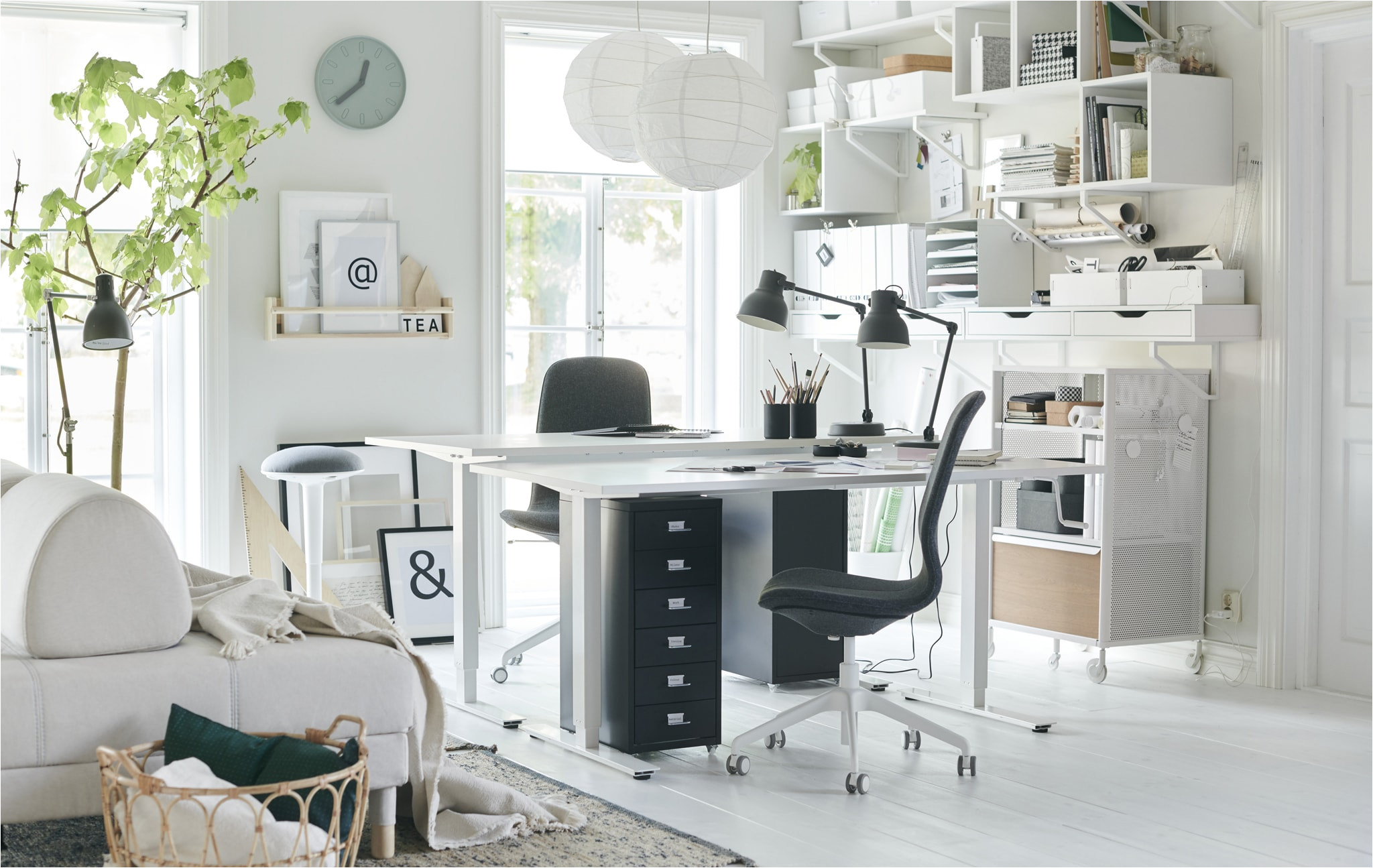 two desks and desk chairs in the corner of a white living room with wall storage