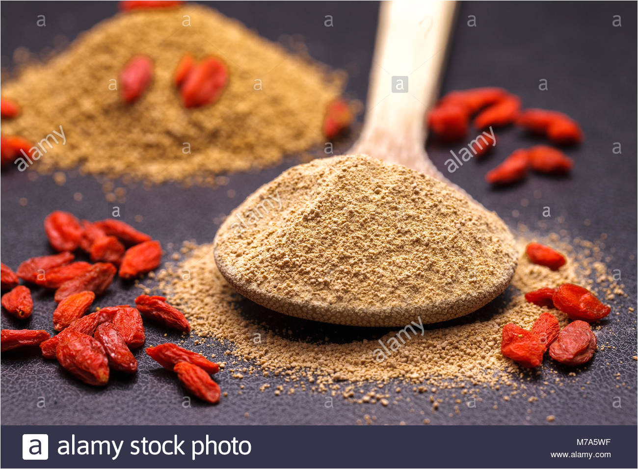 ground up pure cane sugar on a wooden spoon and red goji berries stock