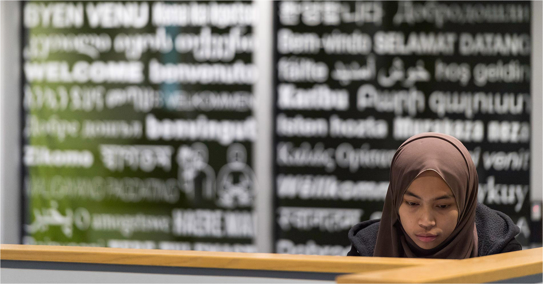 student sits and works in front of a window covered with the word welcome written in