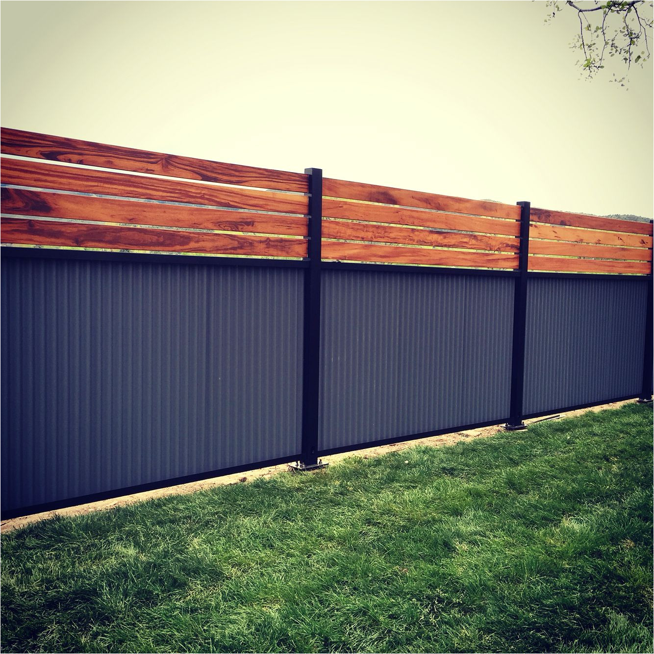 custom privacy fence built out of metal post tiger wood and corrugated metal