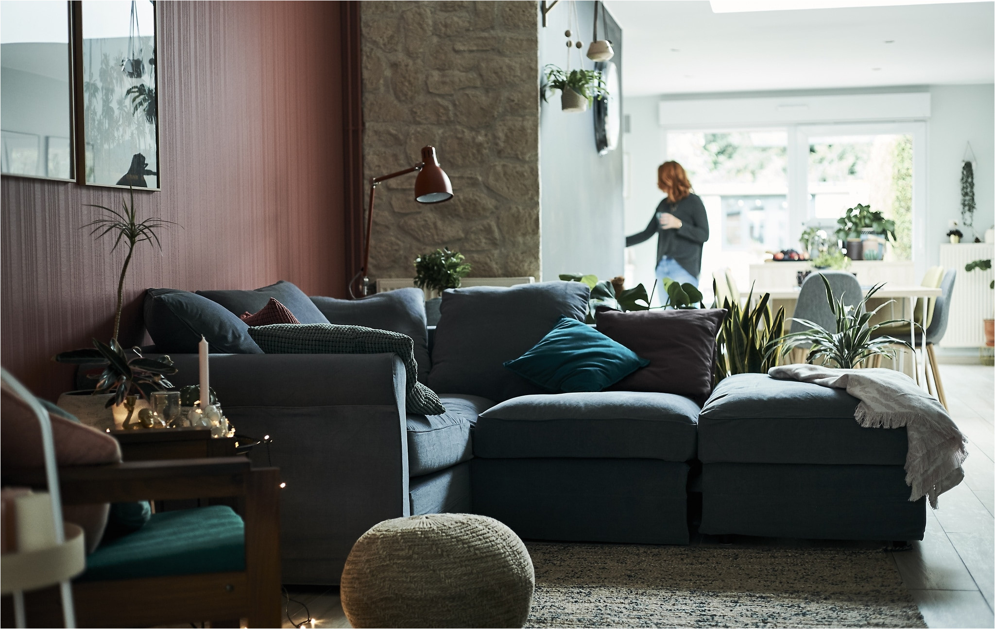 a living room with l shaped grey sofa and red wall with a dining