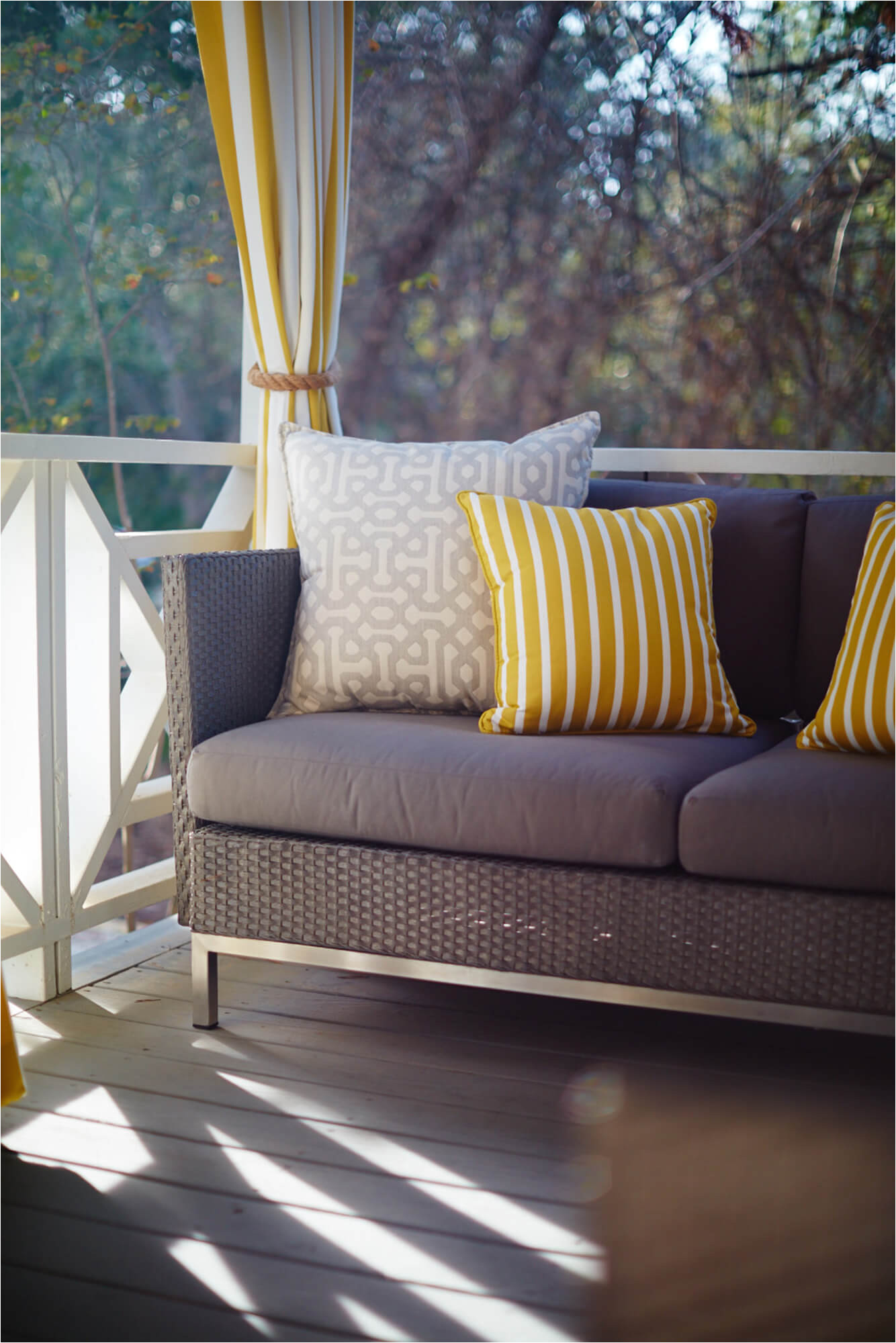 outdoor sofa with yellow and grey decorative throw pillows and yellow and white striped drapery outdoor drapery in